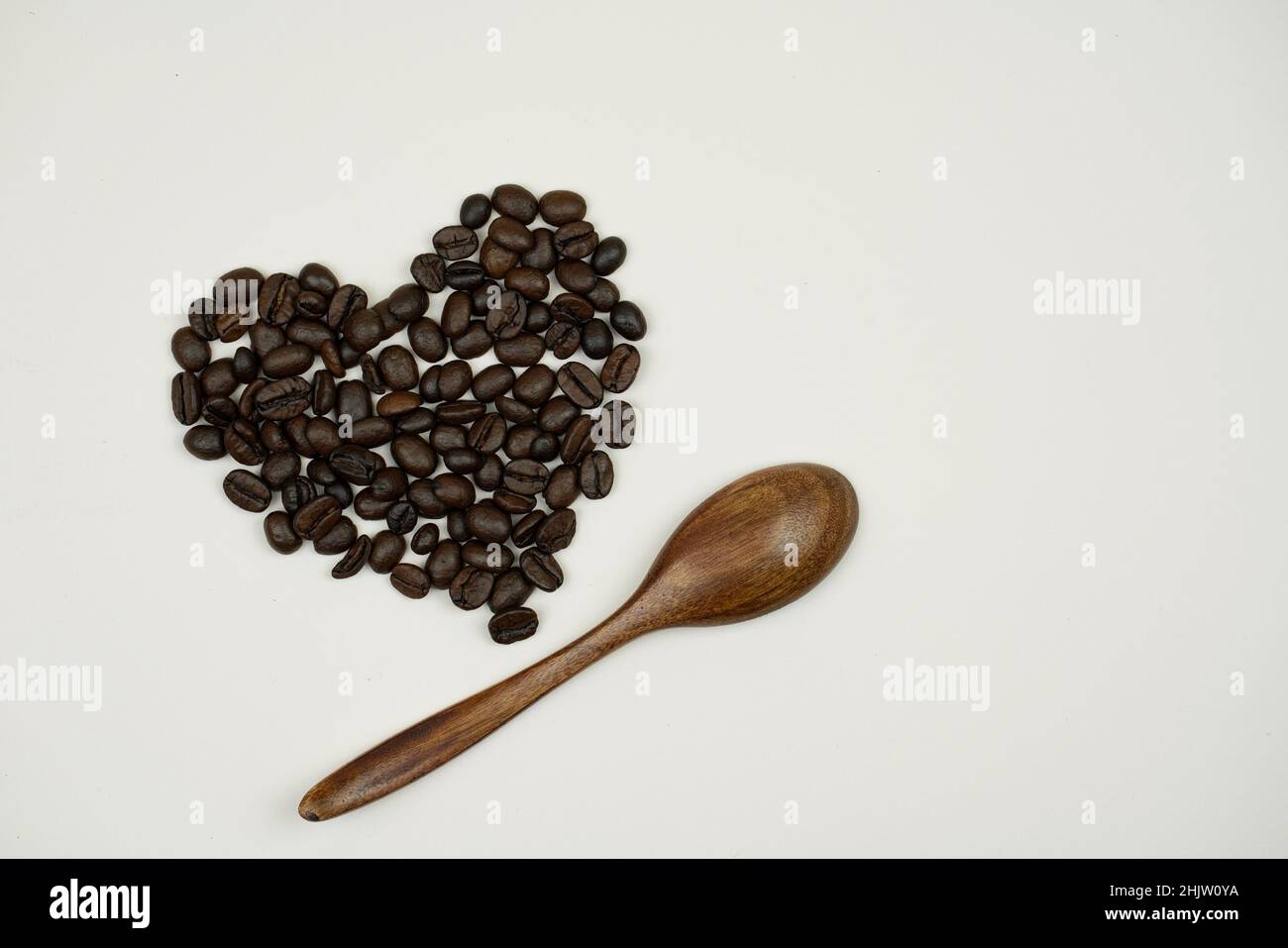 coffee beans in the shape of a heart and a wooden spoon next to it on a bluish-gray background Stock Photo