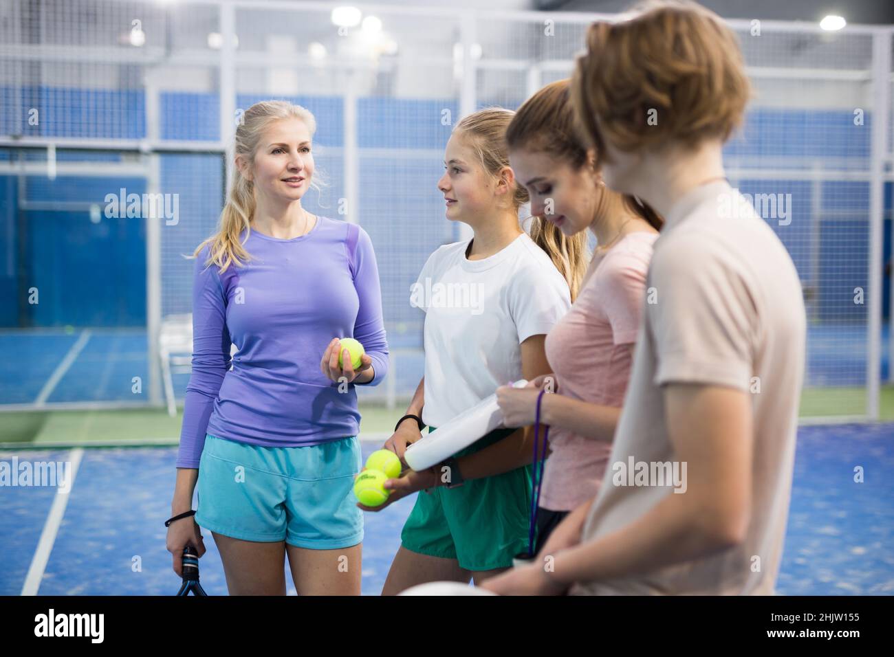 Smiling young man and women with padel rackets posing at court inside Stock Photo