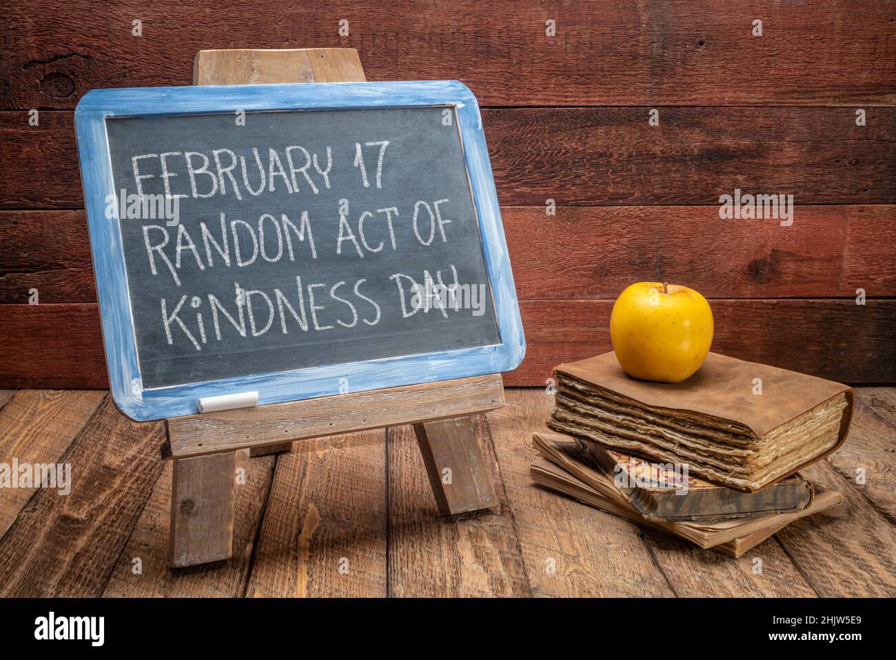 random act of kindness day inspirational reminder  - white chalk handwriting on a vintage slate blackboard with old books against rustic wood backgrou Stock Photo