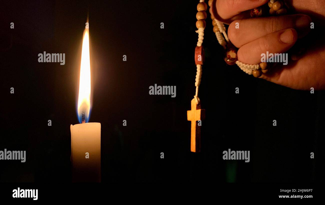 Christian prayer - Holy Rosary and candle with night background. Christian concept. Stock Photo