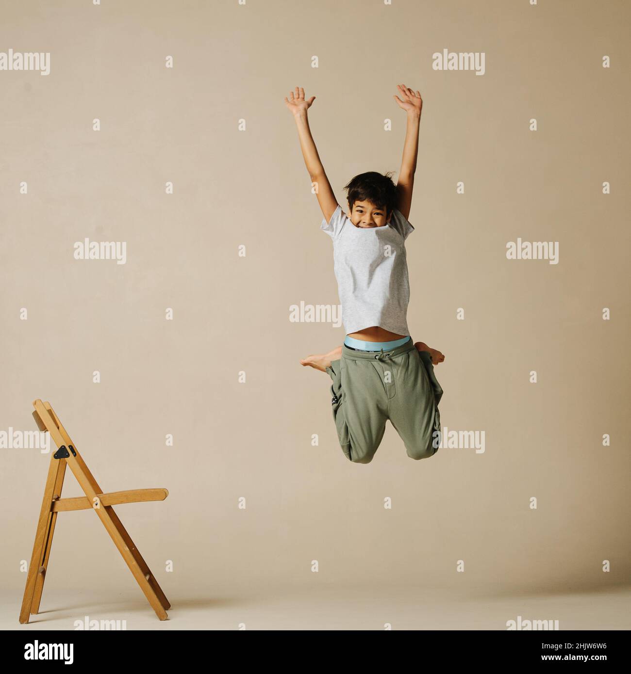 Unsure indian boy jumping up, bending knees and throwing hands up in