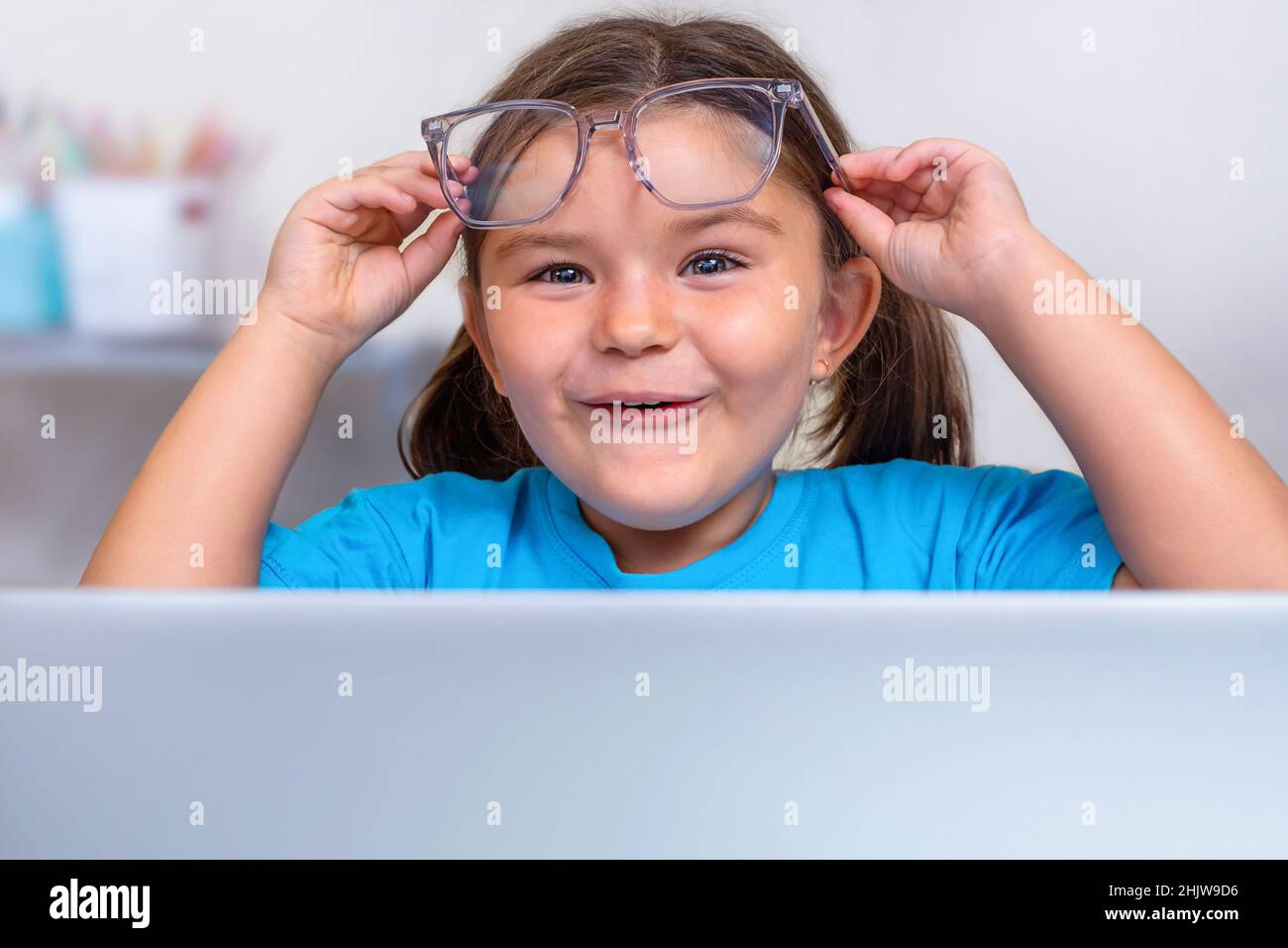 Portrait of the child in eyeglasses peeking in surprise from behind a laptop Stock Photo