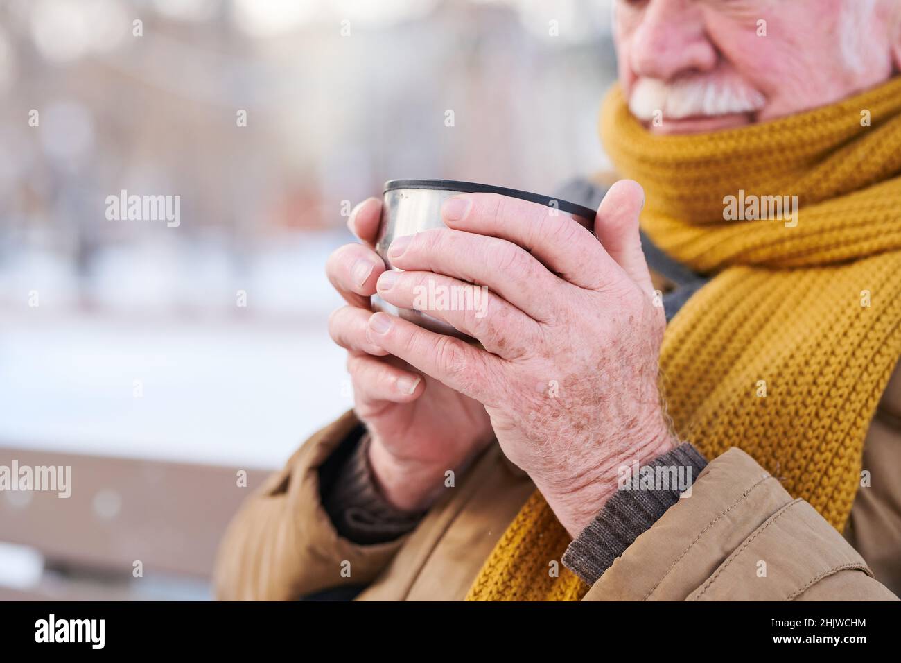 Close-up of senior man holding cup with hot tea in his hands, he warming up during cold weather outside Stock Photo
