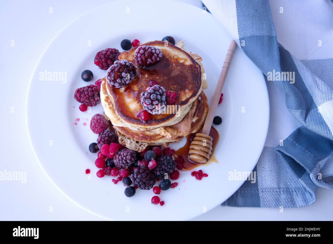 Pancakes with berries and honey on white table Stock Photo