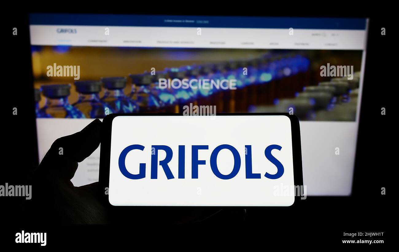 Person holding cellphone with logo of Spanish pharmaceutical company Grifols SA on screen in front of business webpage. Focus on phone display. Stock Photo