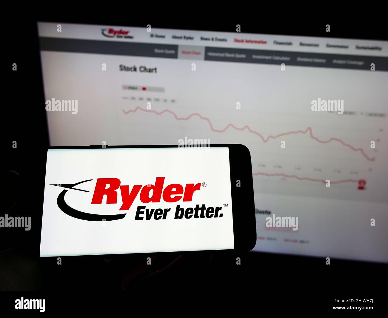 Person holding cellphone with logo of US transportation company Ryder System Inc. on screen in front of business webpage. Focus on phone display. Stock Photo