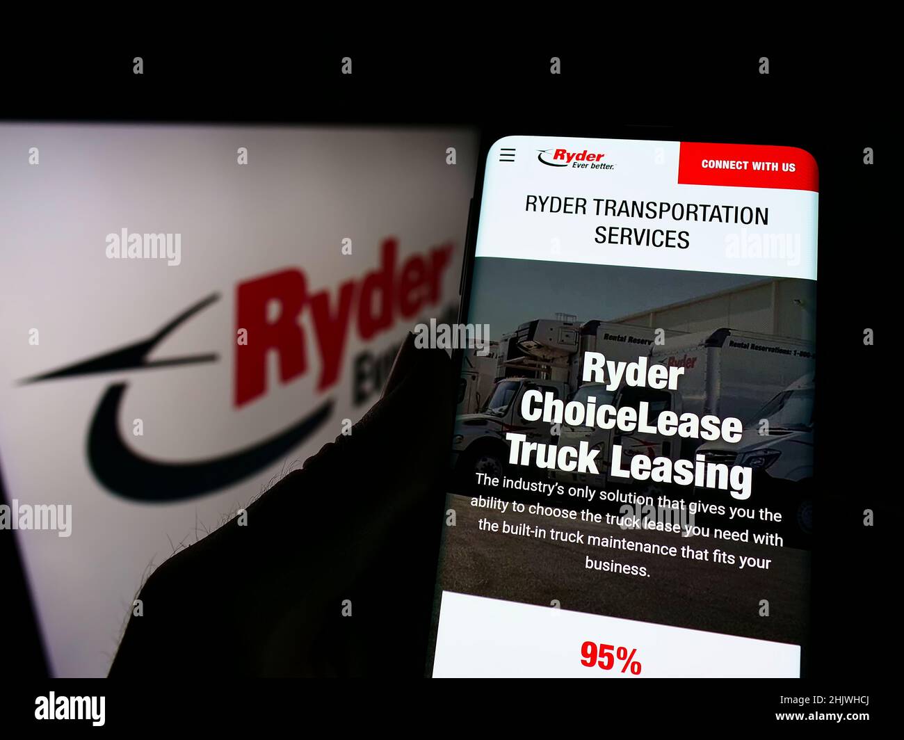 Person holding cellphone with website of US transportation company Ryder System Inc. on screen in front of logo. Focus on center of phone display. Stock Photo