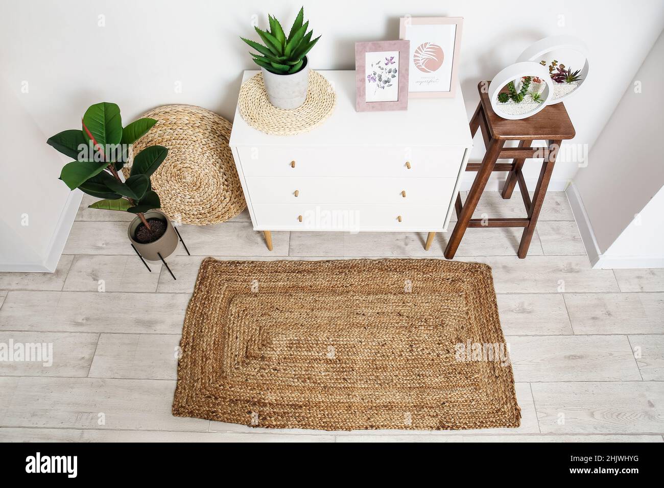 Interior of room with chest of drawers, houseplants and wicker rug ...
