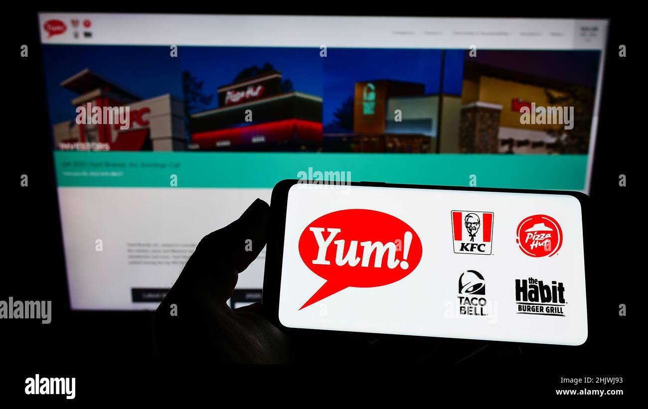 Person holding smartphone with logo of US fast food company Yum! Brands Inc. on screen in front of website. Focus on phone display. Stock Photo