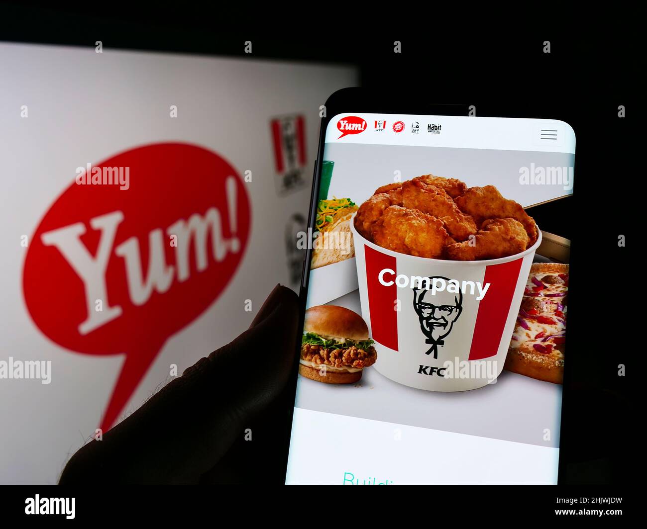 Person holding cellphone with website of US fast food company Yum! Brands Inc. on screen in front of logo. Focus on center of phone display. Stock Photo