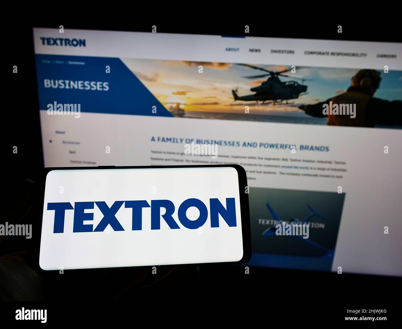 Person holding cellphone with logo of US aerospace company Textron Inc. on screen in front of business webpage. Focus on phone display. Stock Photo
