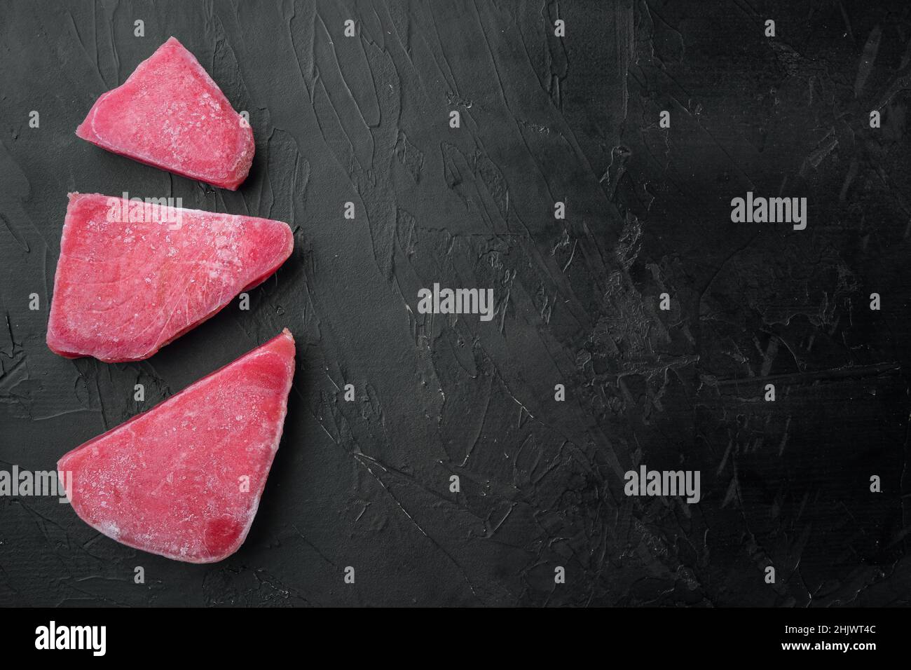 Raw frozen tuna fish fillet set, on black stone background, top view