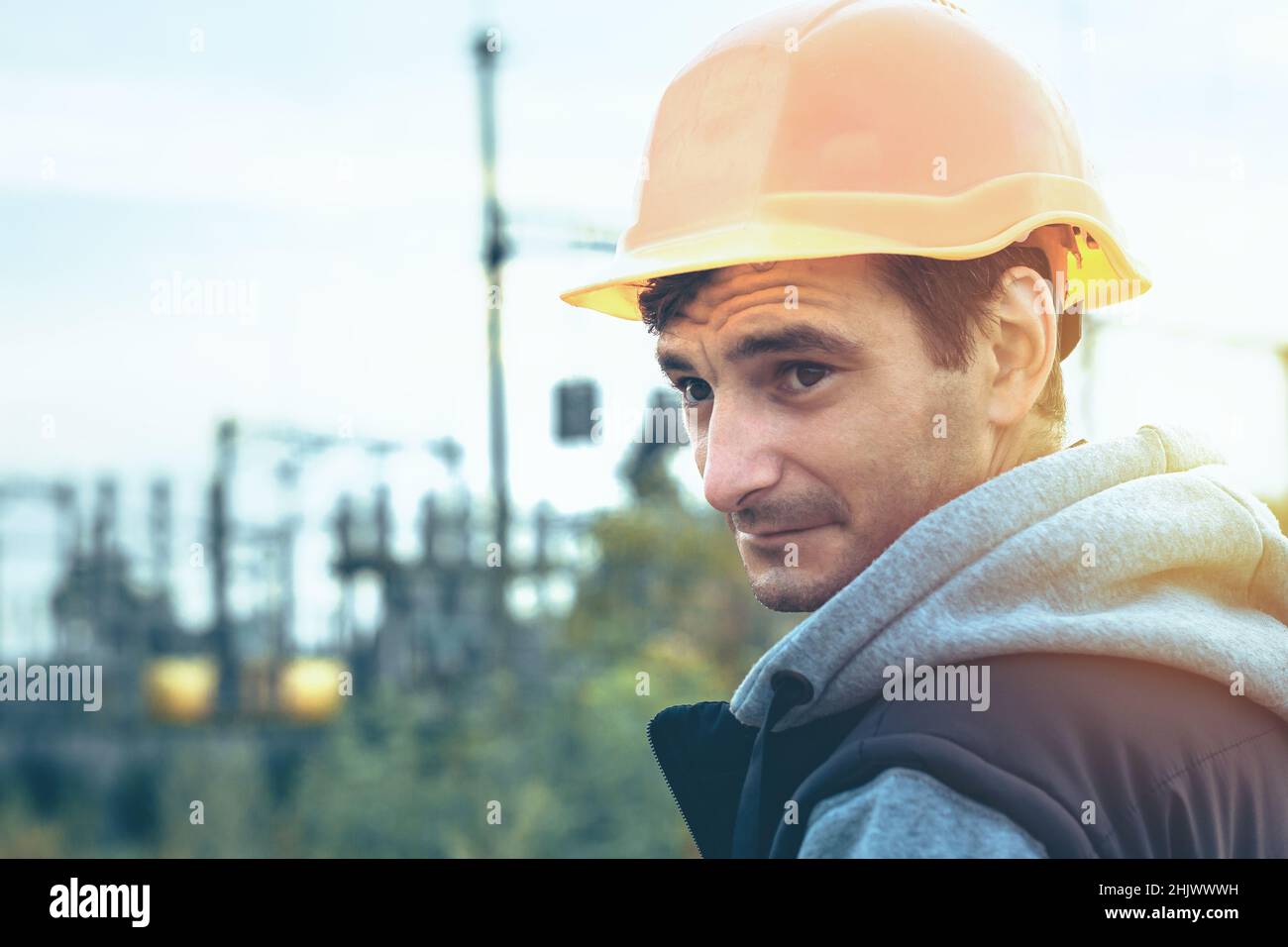 Worker in a helmet against the background of a substation and high-voltage poles Stock Photo