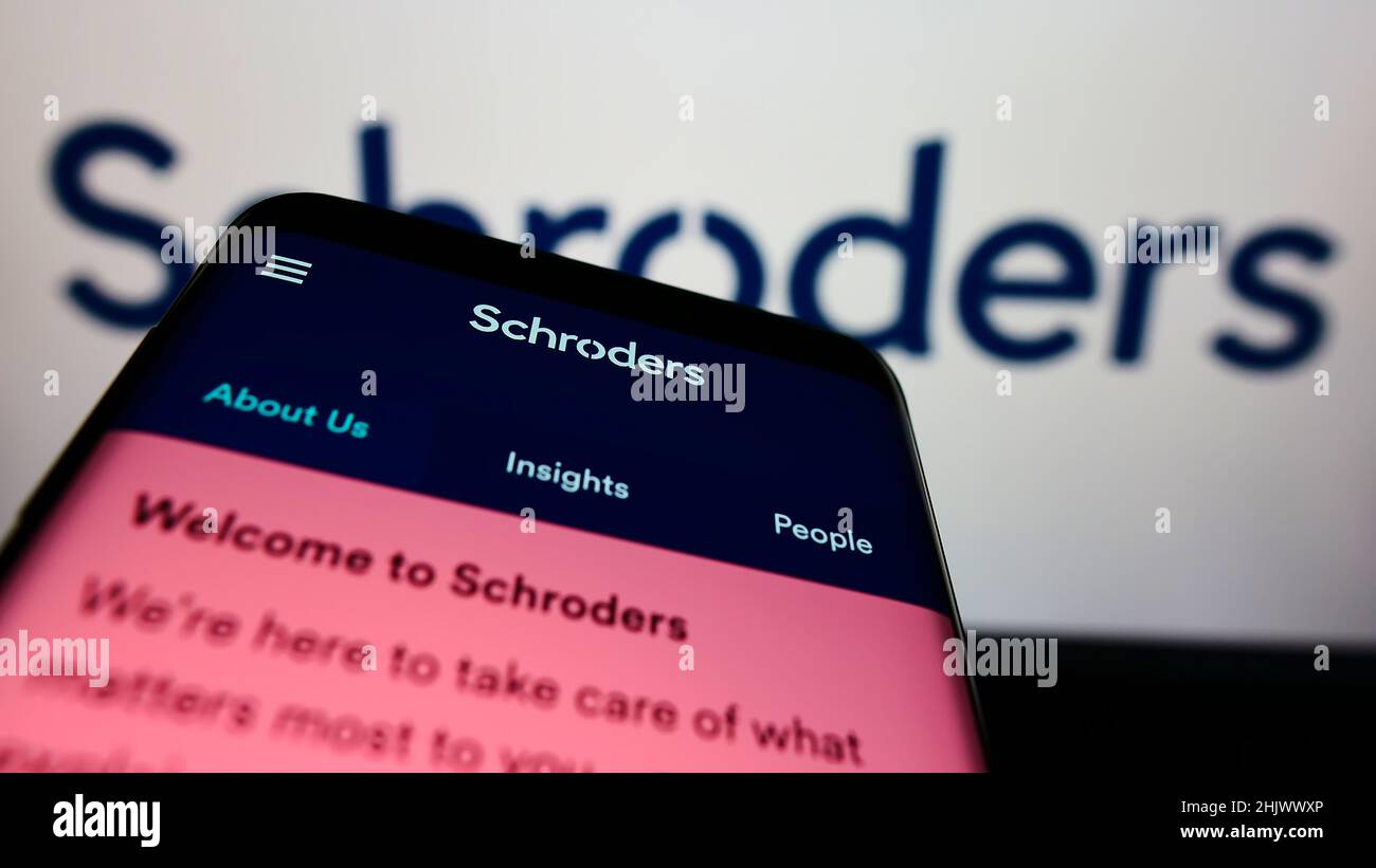 Smartphone with website of British asset management company Schroders plc on screen in front of business logo. Focus on top-left of phone display. Stock Photo