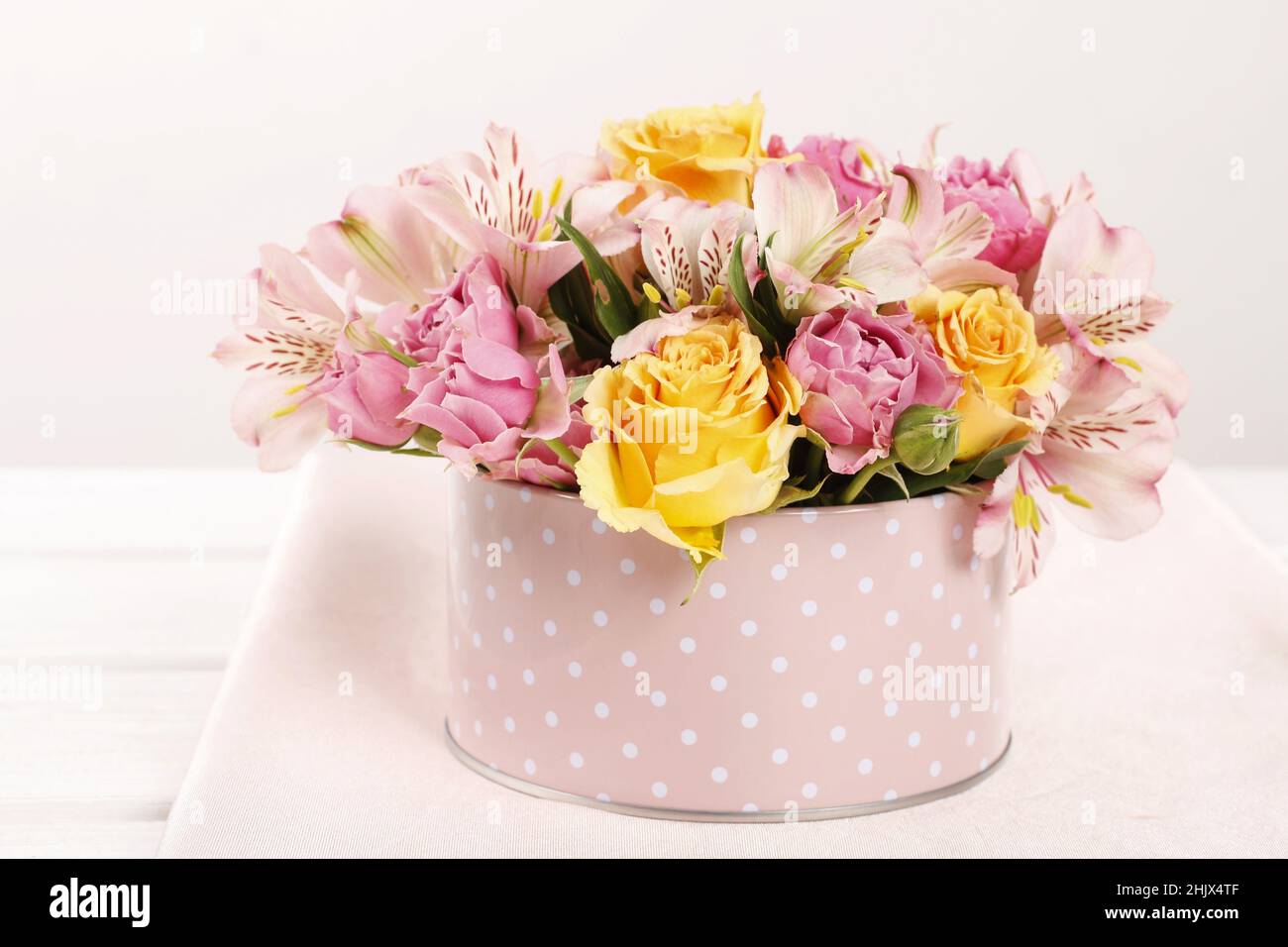 Florist at work: woman shows how to make floral arrangement with roses and other flowers inside a pink dotted can. Step by step, tutorial. Stock Photo