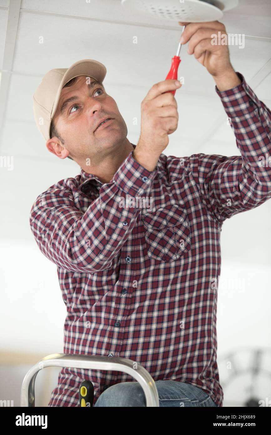 worker installing smoke detector on ceiling Stock Photo
