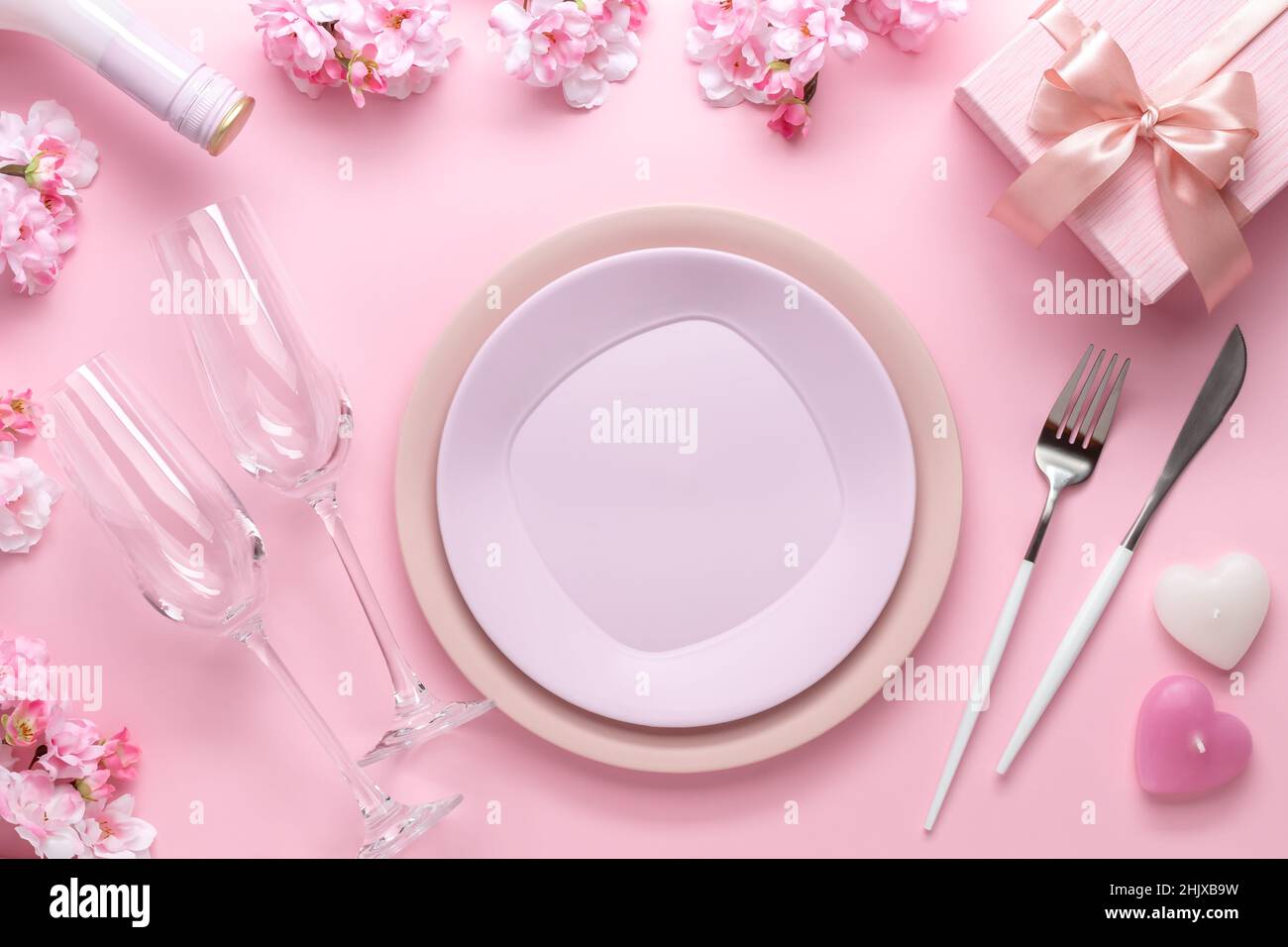 Place setting for Valentine's Day. Romantic dinner, table setting with cutlery. Pink background. Dating concept, love. Spring flowers, empty plate, gl Stock Photo