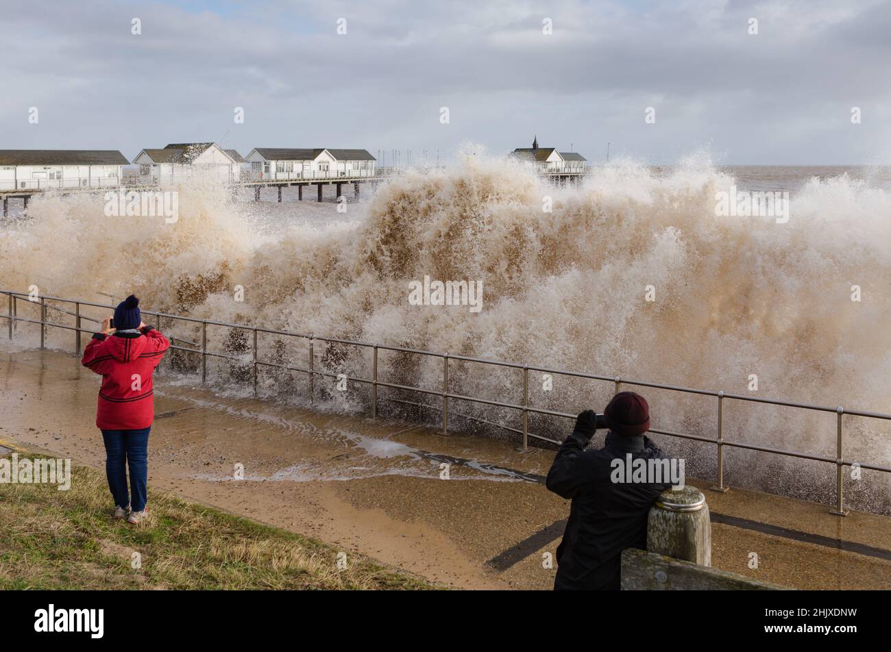 Couple photograph crashing waves at high tide pounding the beach promenade at Southwold Pier Stock Photo