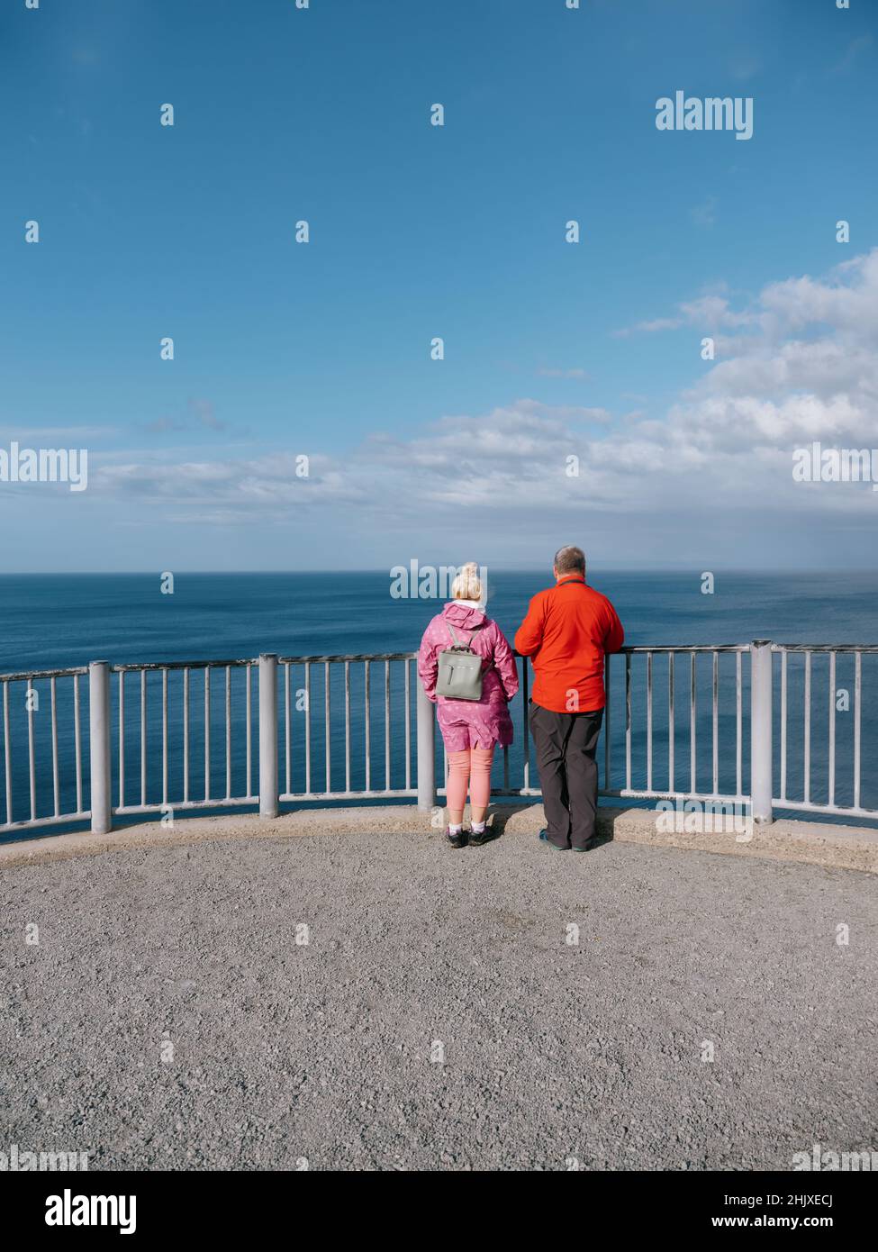 Tourists dressed for the outdoors at a seascape viewpoint with a blue sea sky horizon - Kilt Rock & Mealt Falls Viewpoint, Isle of Skye, Scotland UK Stock Photo
