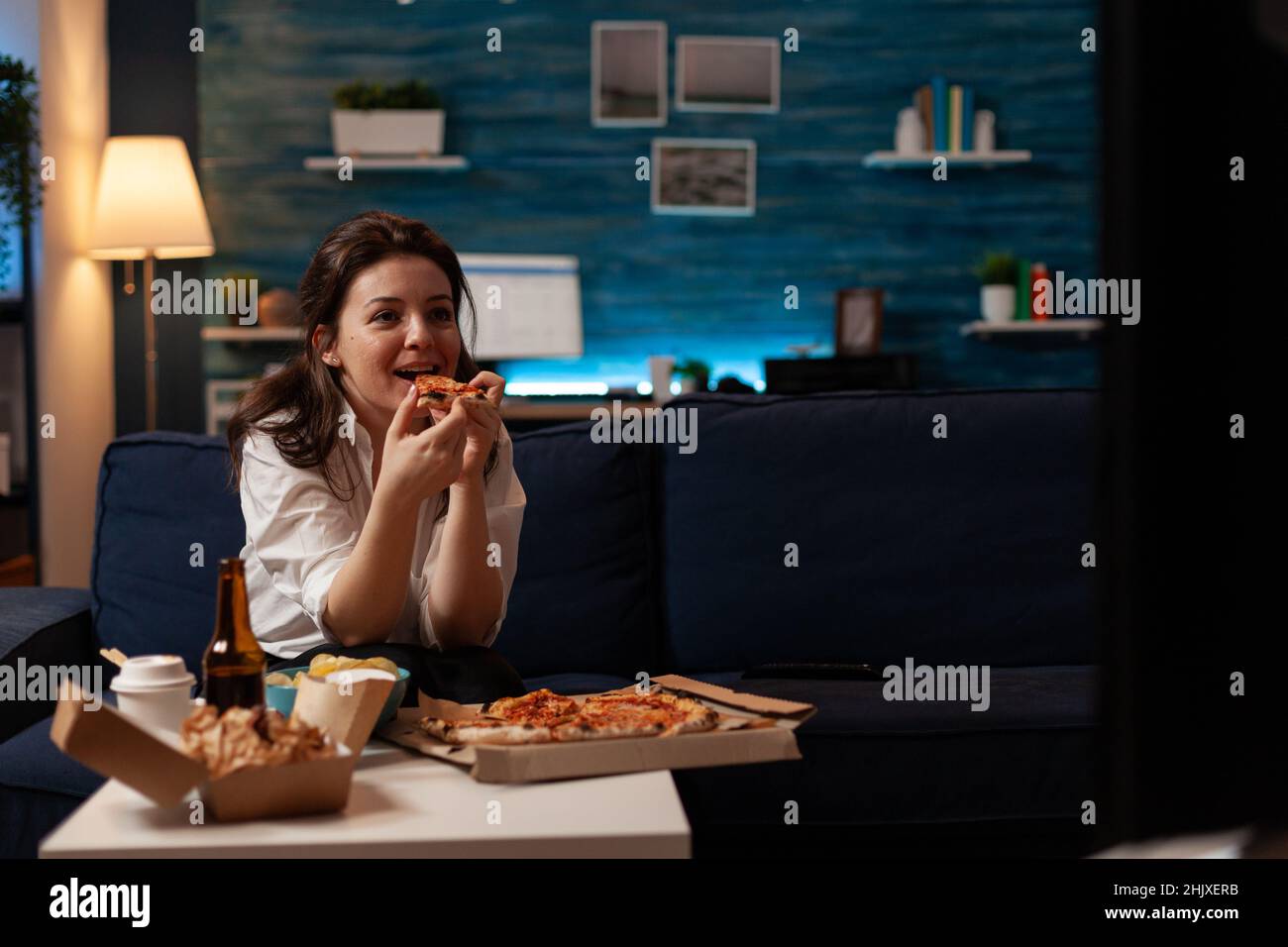 Smiling woman eating a slice of hot pizza delivery sitting on couch