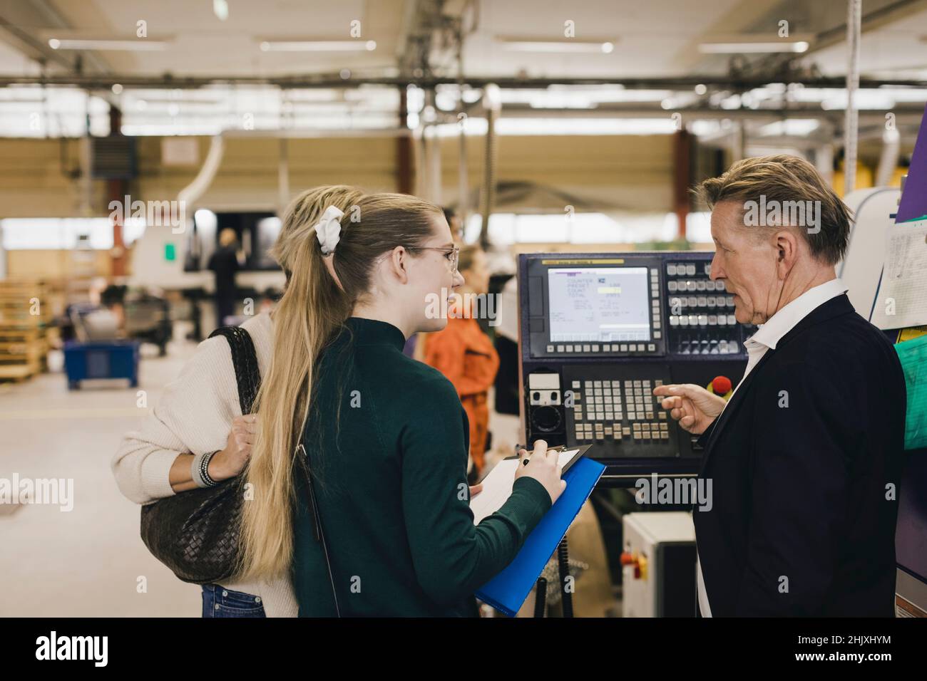 Senior businessman discussing with female manager over manufacturing machinery in factory Stock Photo