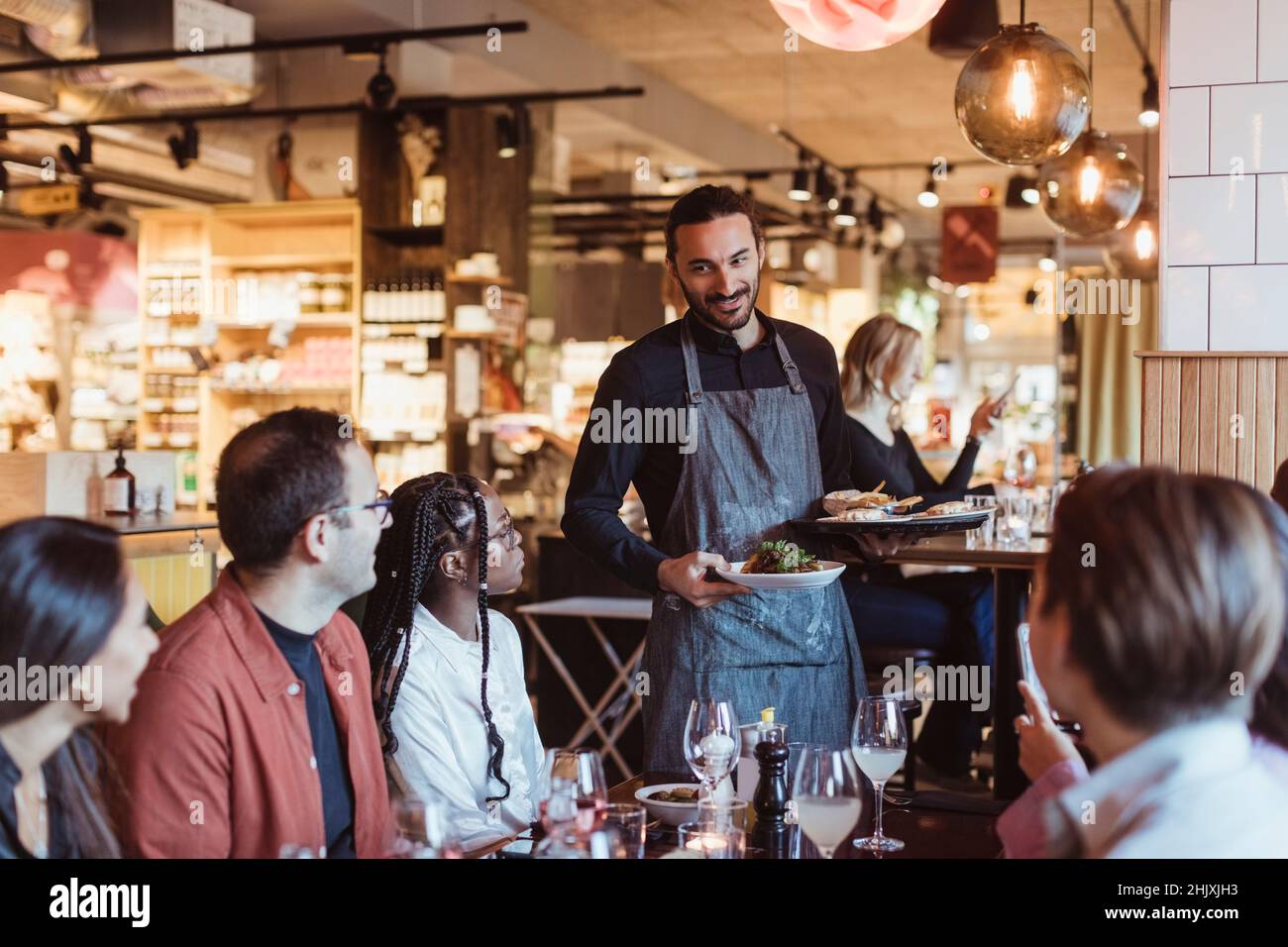 Waiter serving food to multiracial customers during party in restaurant