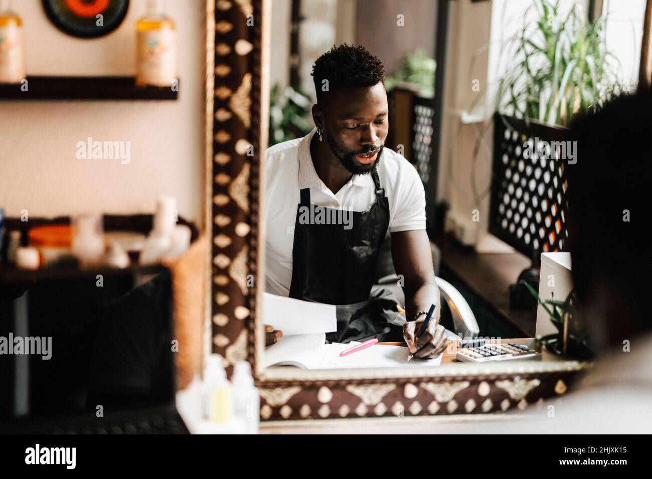 Reflection of male hairdresser calculating financial bill in barber shop Stock Photo