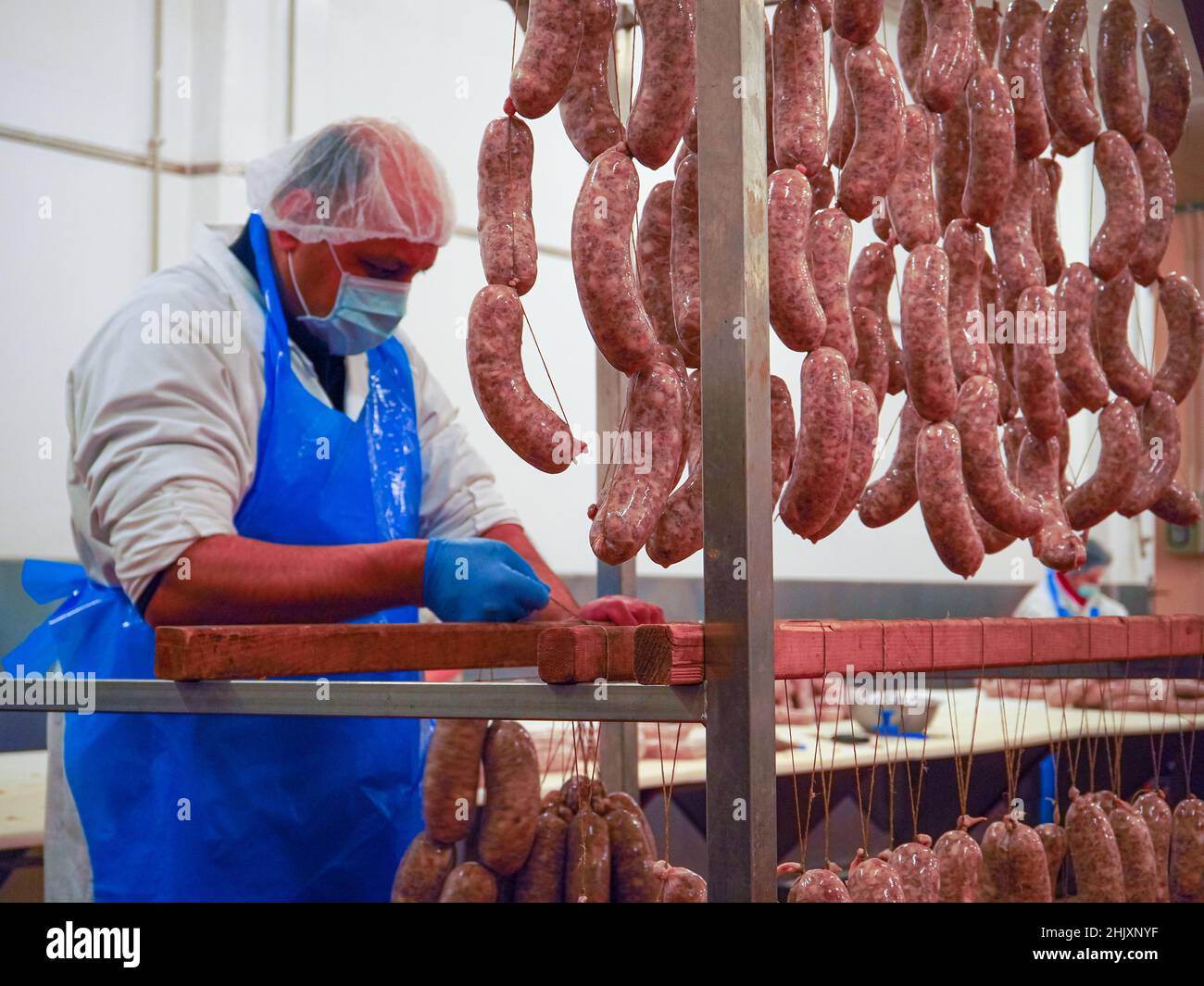 worker manufacturing, stuffing and tying pork sausages, salami and