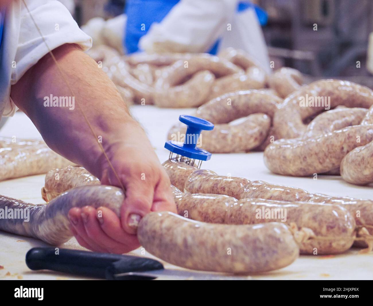 Factory Stuffing worker manufacturing, stuffing and tying pork sausages, salami and ...
