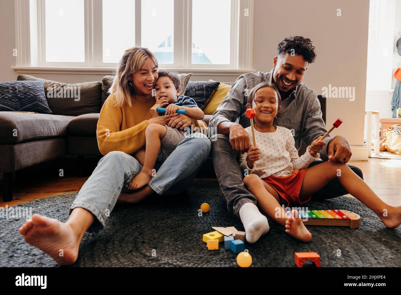 Loving parents playing with their son and daughter in the living room. Mom and dad having fun with their kids during playtime. Family of four spending Stock Photo
