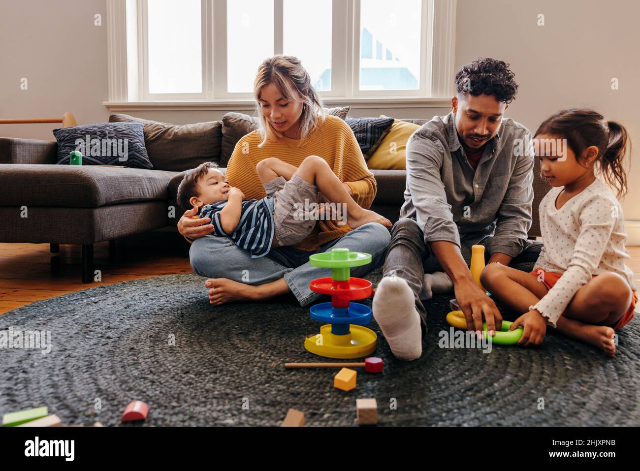 Mom and dad playing with their kids in the living room at home. Two young parents having fun with their son and daughter during playtime. Family of fo Stock Photo
