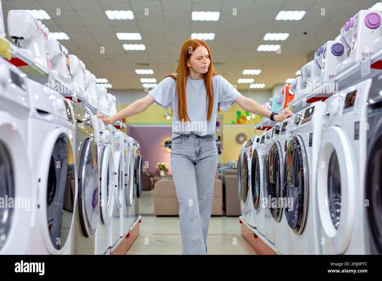 Hard decision.Redhead lady choosing between two washing machines ...