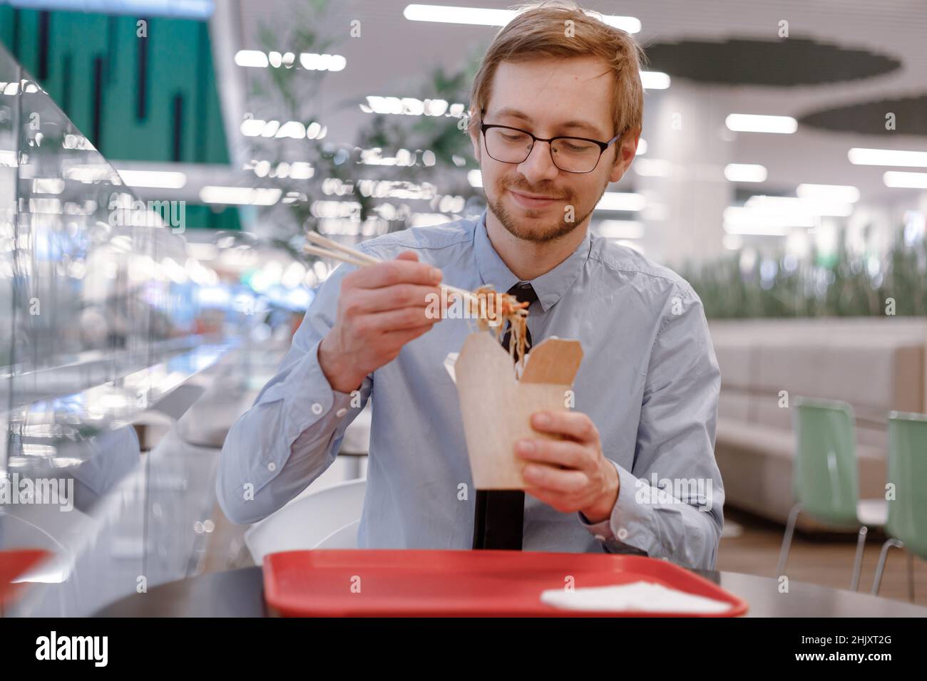Hungry man trader in shirt eating chinese wok from box on food court. Lunch break. Stock Photo