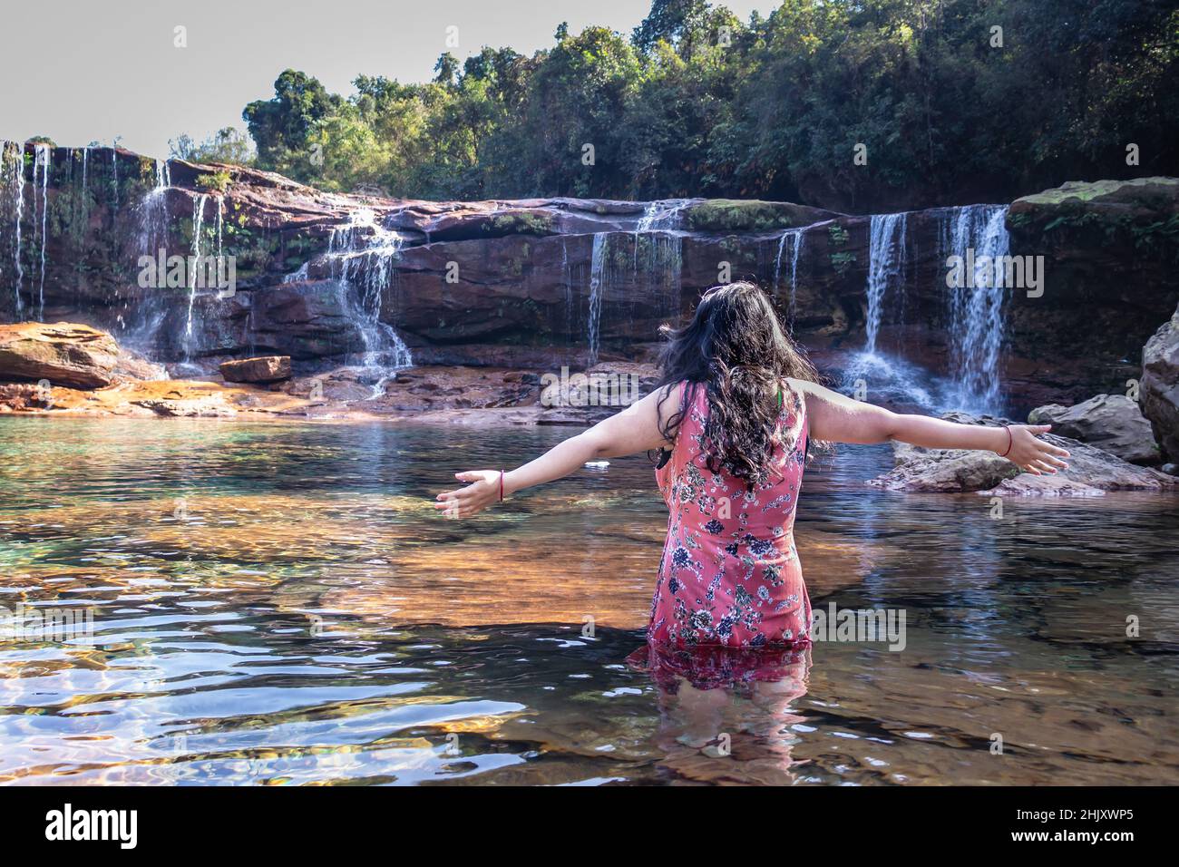 girl standing with waterfall flowing streams and calm clear water at morning image is taken at mawasawa waterfall cherrapunji meghalaya india. Stock Photo