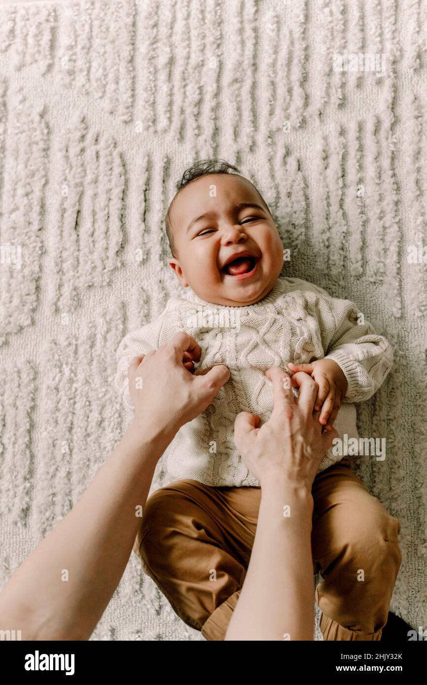 Cropped image of mother tickling baby boy lying on blanket Stock Photo