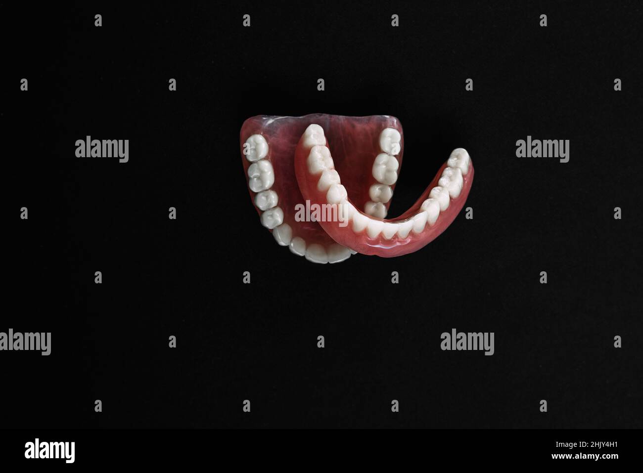 Full removable plastic denture of the jaws. A set of dentures on a black background. Two acrylic dentures. Upper and lower jaws with fake teeth. Dentu Stock Photo