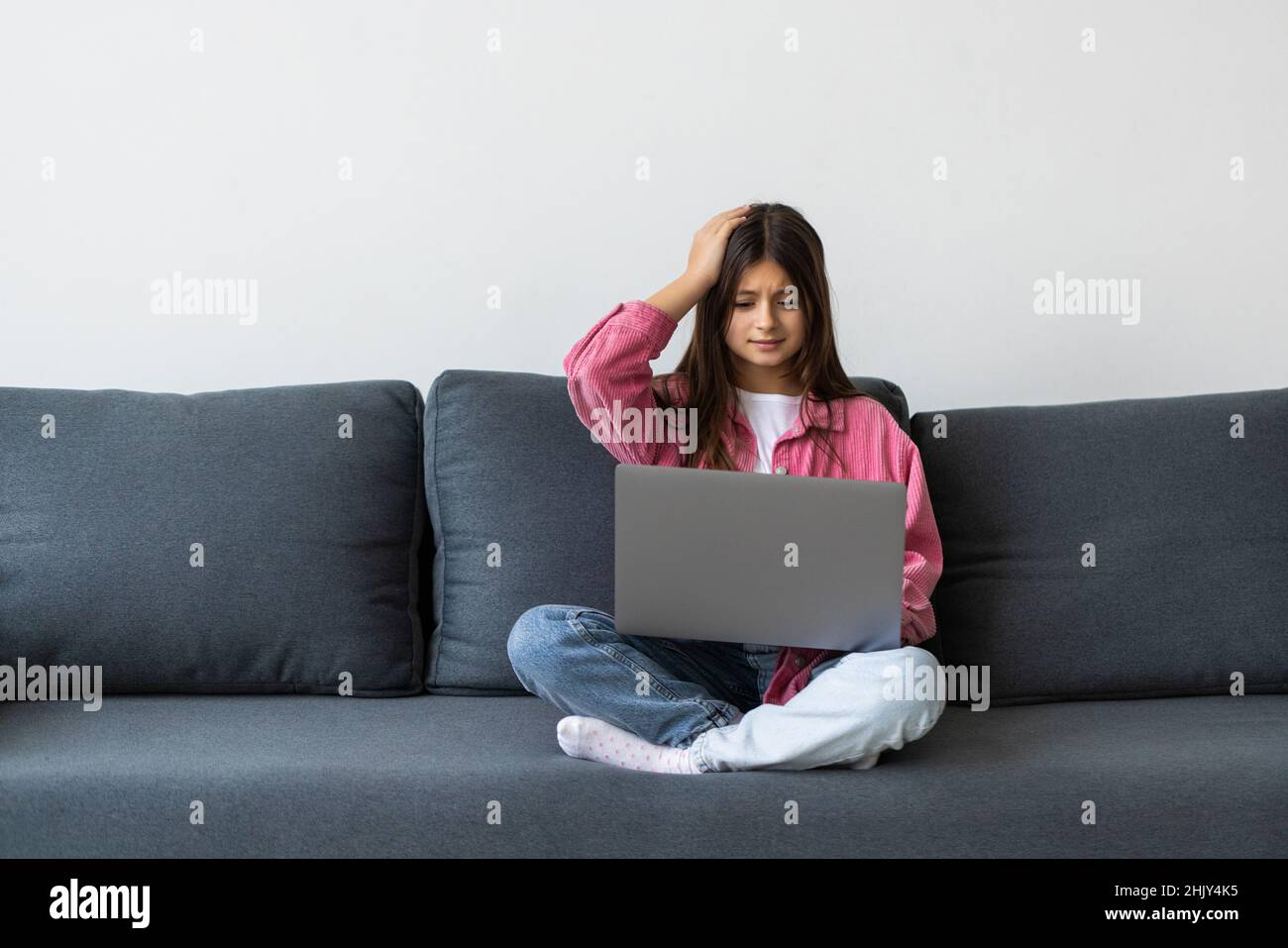 young girl sitting on sofa at her home and using computer for online ...