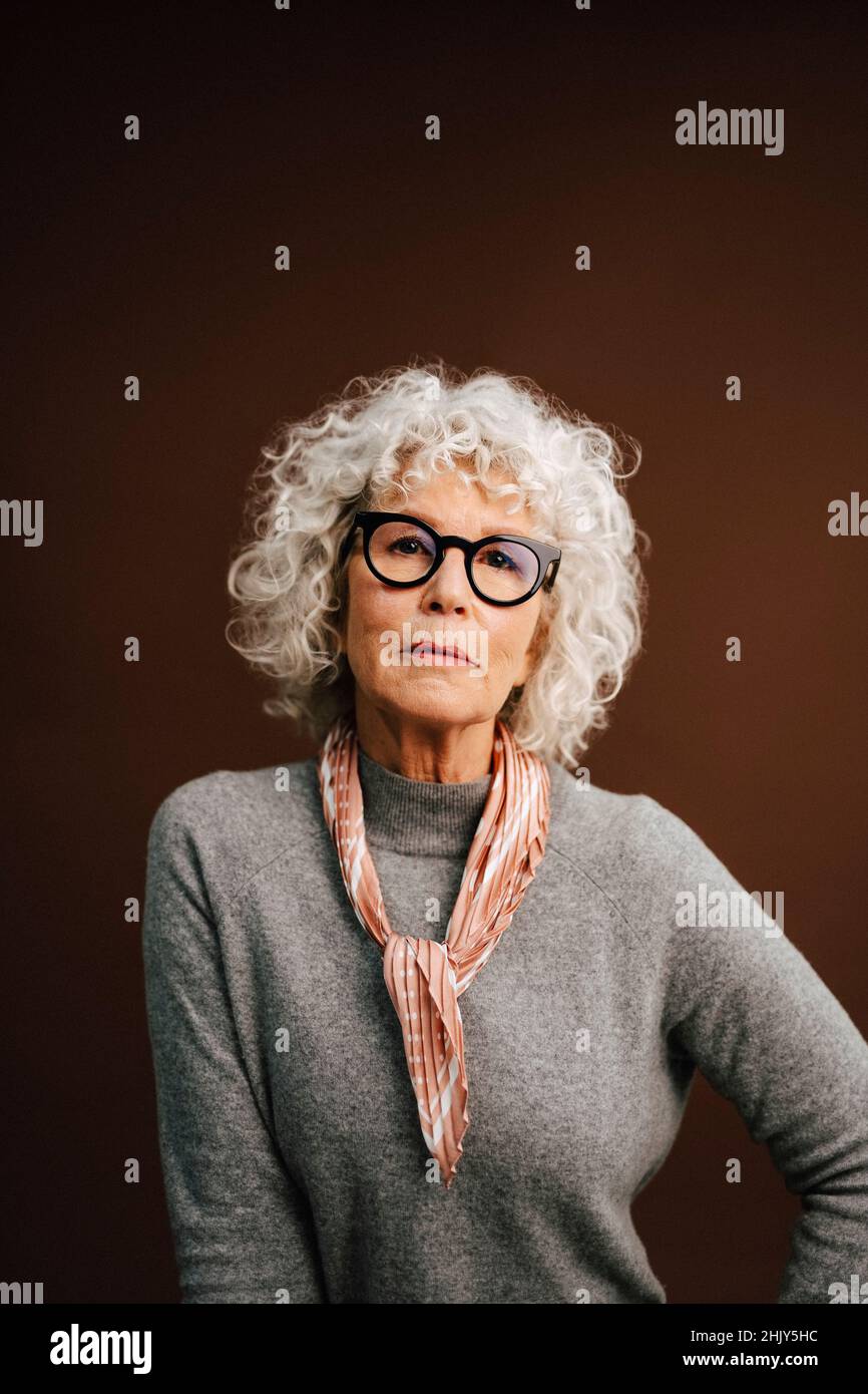 Portrait of elderly woman wearing eyeglasses over brown background Stock Photo