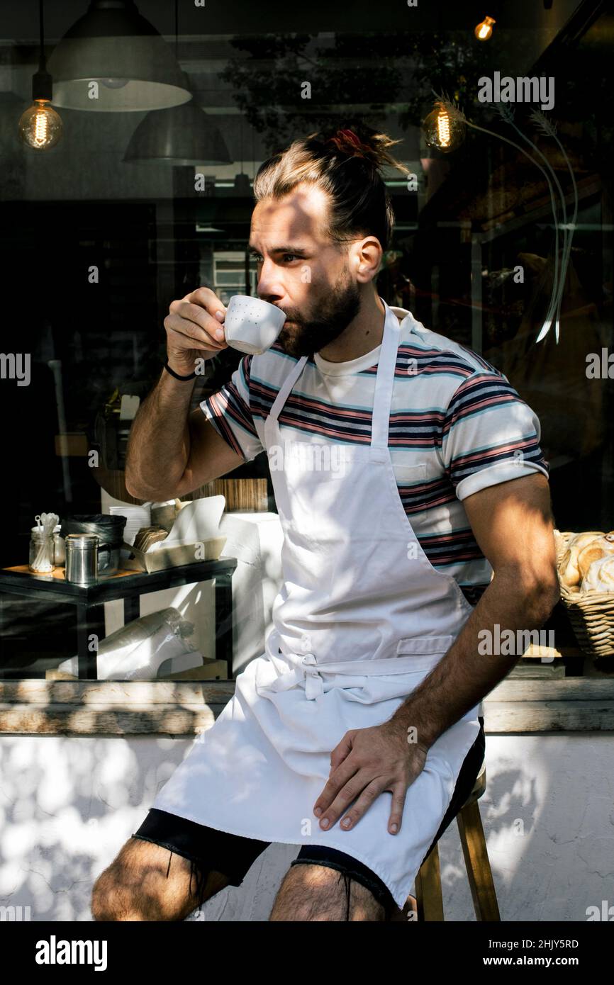 Young male owner drinking coffee while sitting outside cafe Stock Photo