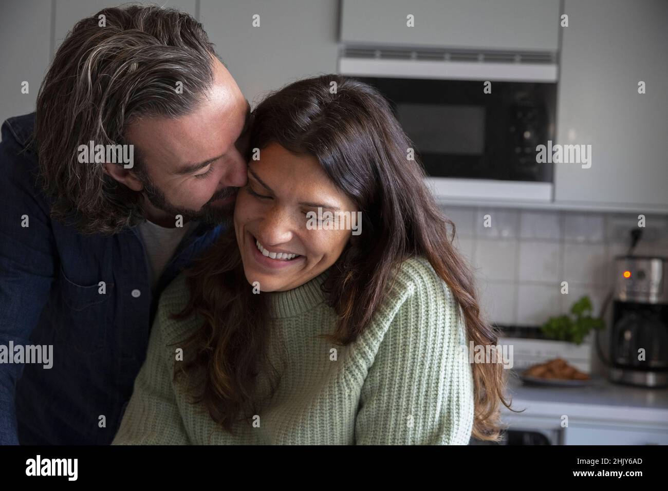 Happy man kissing woman in kitchen Stock Photo