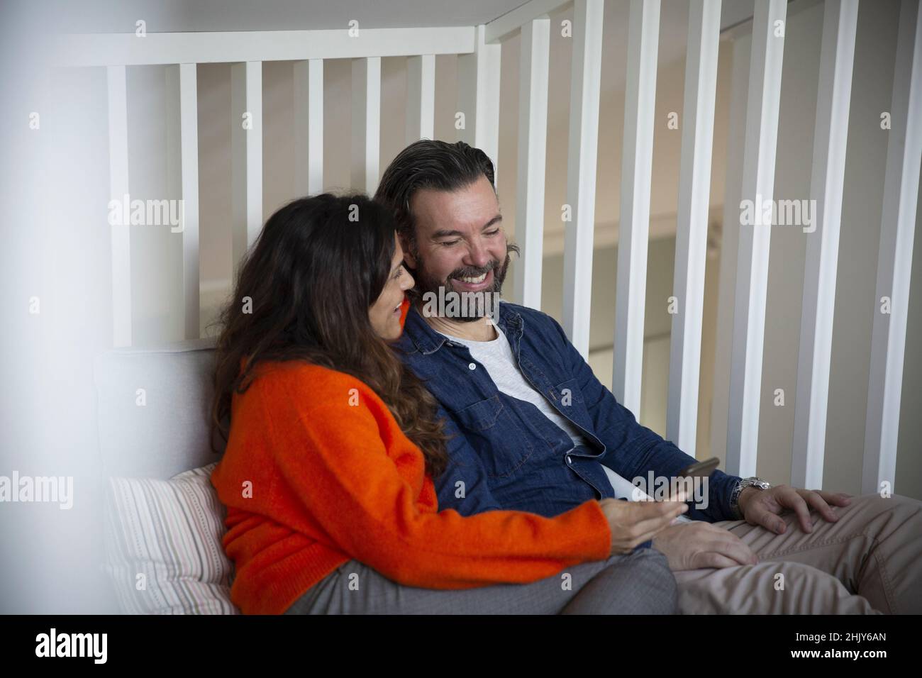Happy heterosexual couple using smart phone in bedroom Stock Photo