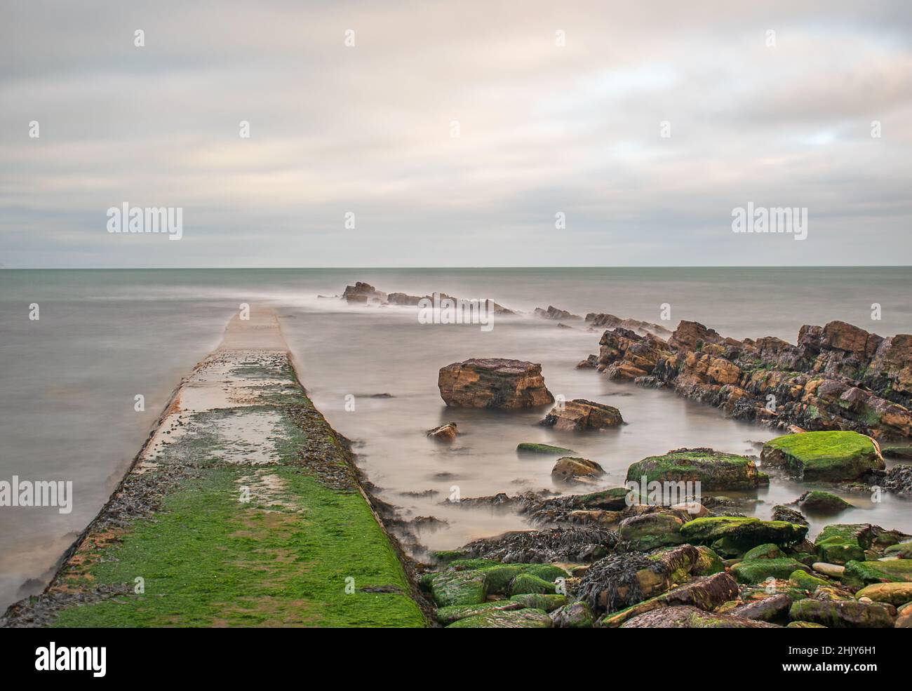 A slow shutter exposure of the sunken walkway at Swanage Peveril Point and the rocks in the still milky sea Stock Photo