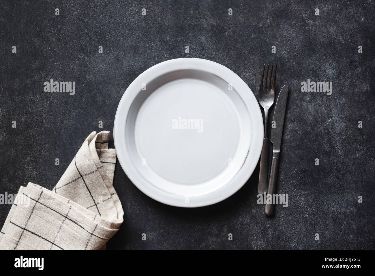 Empty plate, cutlery and linen table textile on black concrete table background. Top view copy space. Kitchen table setting Stock Photo