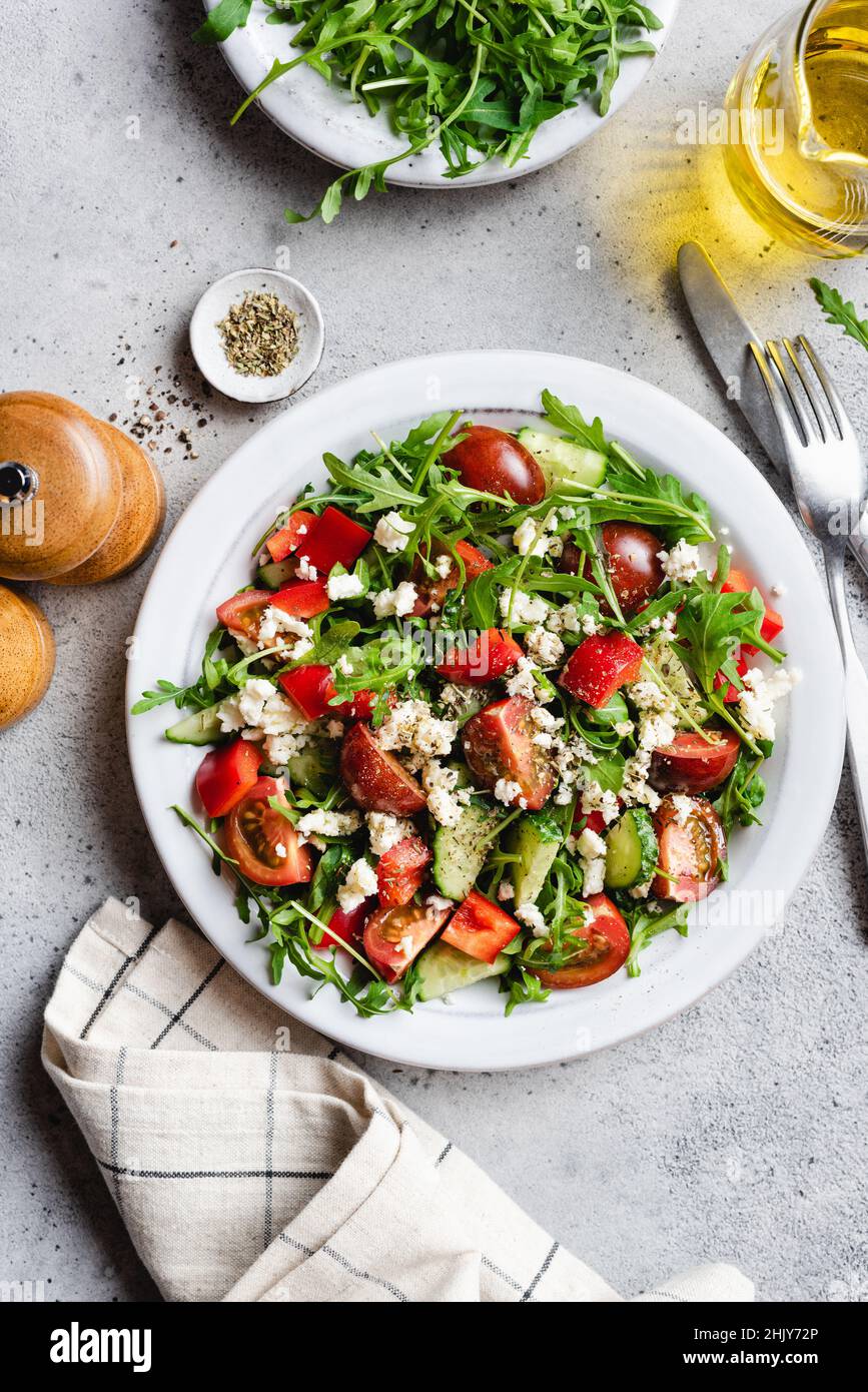 Healthy vegetarian salad with tomatoes, arugula and goats feta cheese on a plate dressed with olive oil. Table top view Stock Photo
