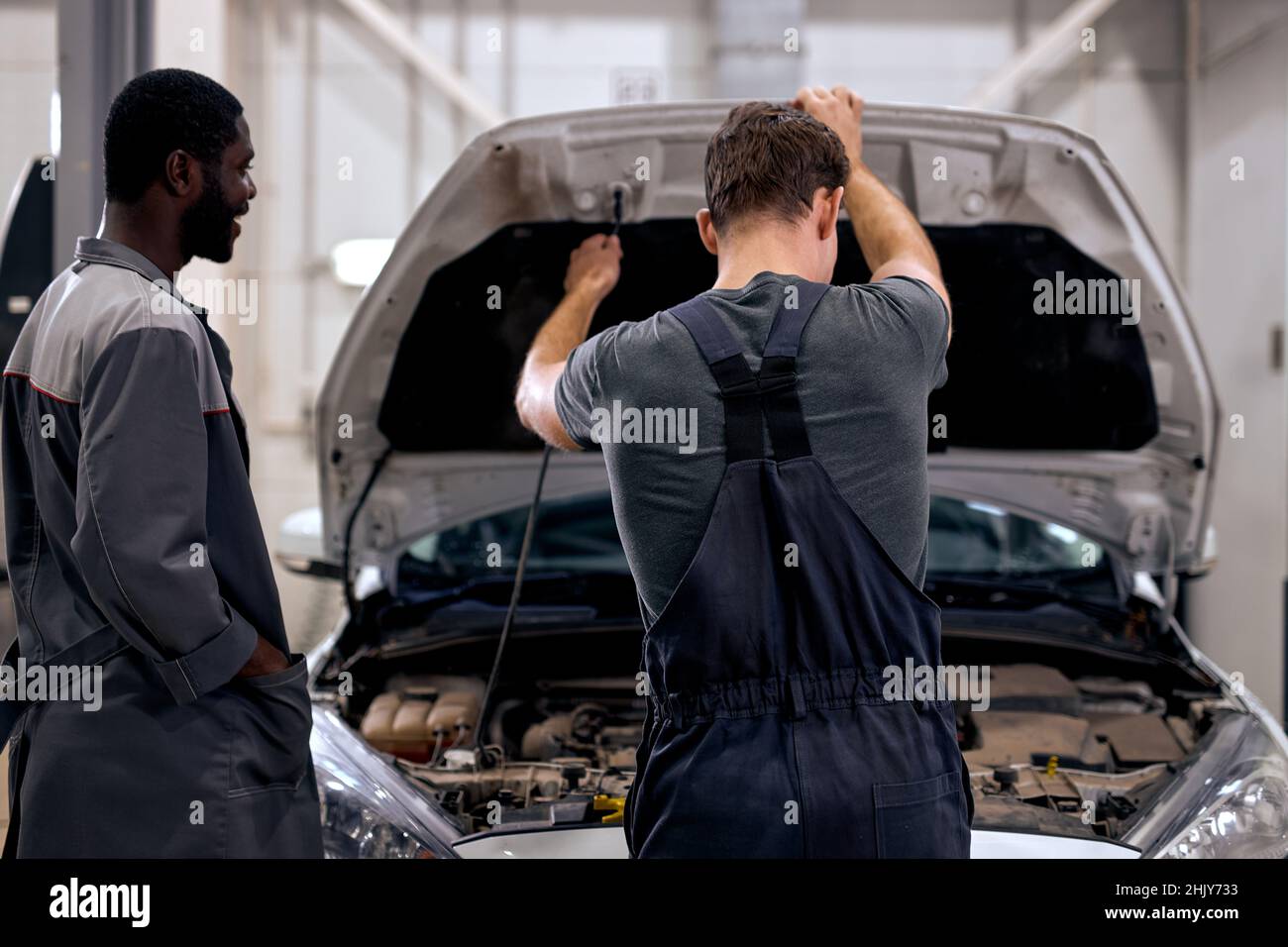 black and american or caucasian men can fix anything. handsome car mechanics  in overalls uniform checking the engine under hood in modern clean car se  Stock Photo - Alamy