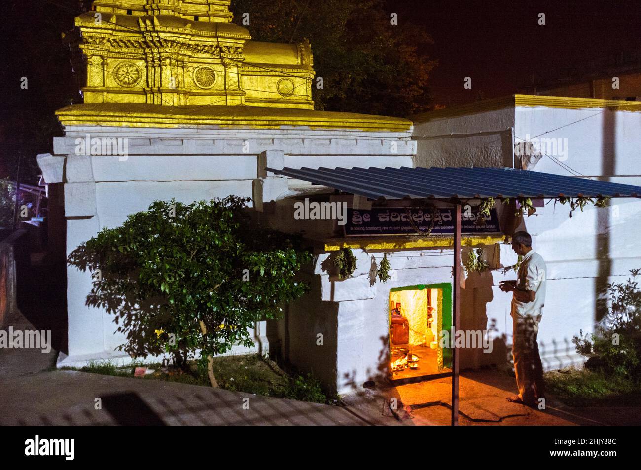 Belur, Karnataka, India : A man stands on prayer before a small shrine in the street at night. Stock Photo