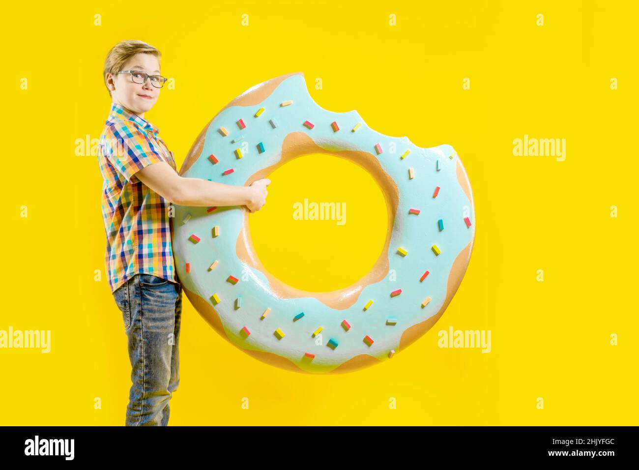 A cute boy is holding a huge donut in his hands. Cheerful teenager. Confectionery. Delicious dessert. A guy with a funny face. Side view Stock Photo