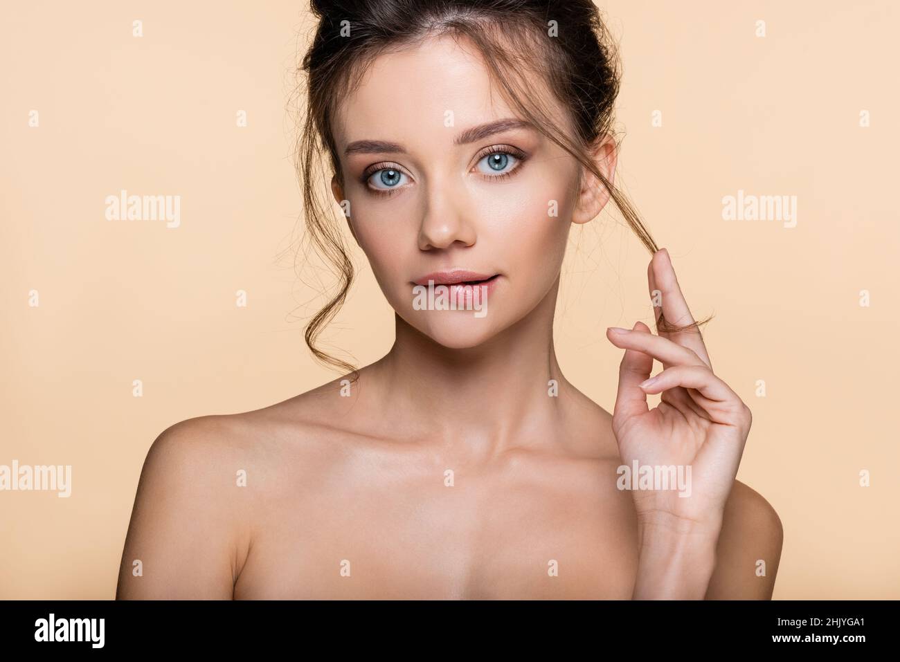 Pretty model touching hair and biting lip isolated on beige Stock Photo