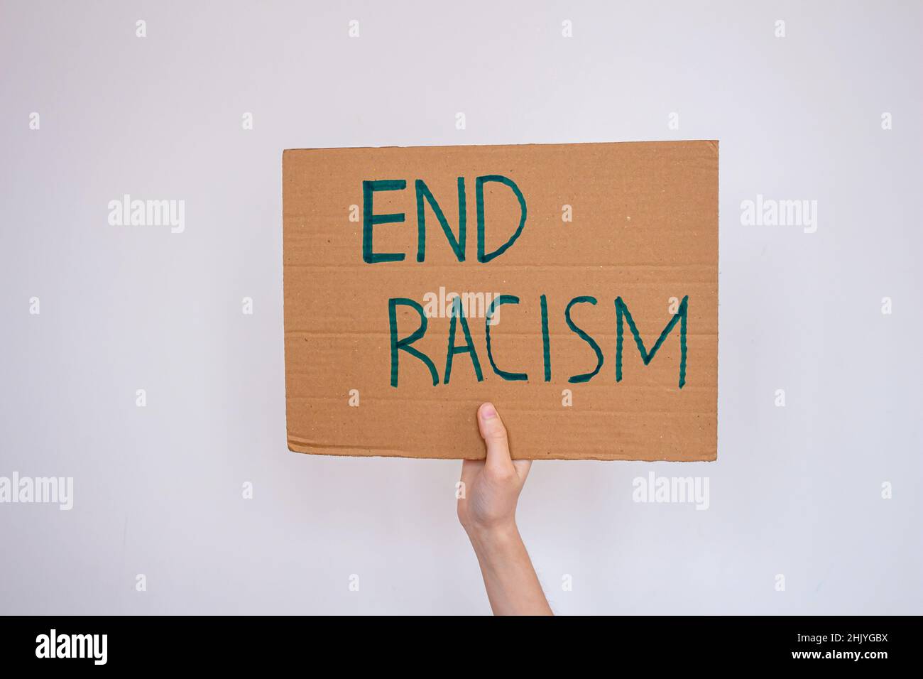 Hand holding cardboard with 'end racism' inscription over gray wall background. Woman is protesting racism. Stock Photo