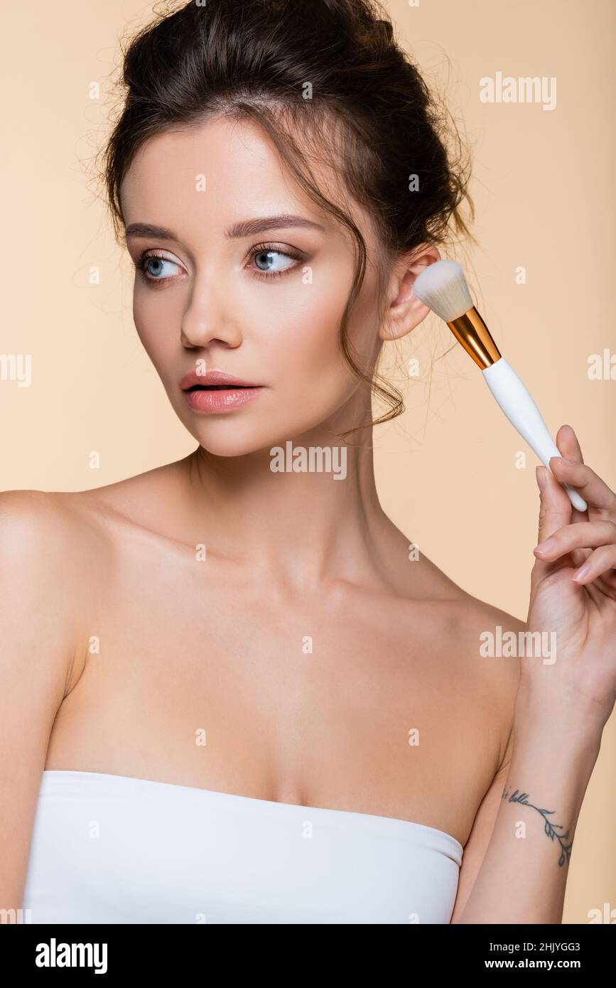 Pretty model in top holding cosmetic brush isolated on beige Stock Photo